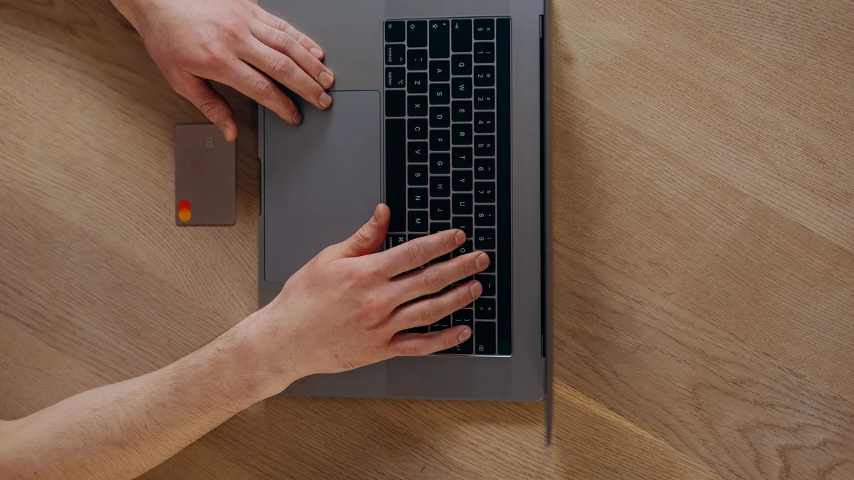 Hands filling in an online form to borrow 300 dollars on a laptop with a bank card beside it