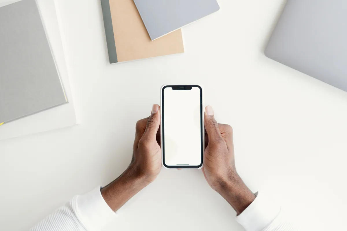 Hands holding a phone over a desk with notebooks and a laptop, ready to apply online, the first step in how to get a small loan in Canada