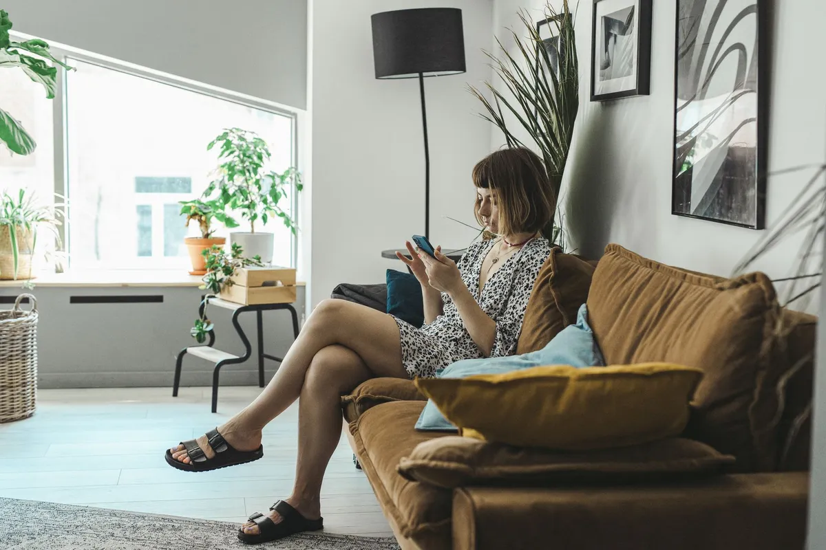 Woman on her couch at home checking a loan app on her phone before deciding on a micro loan