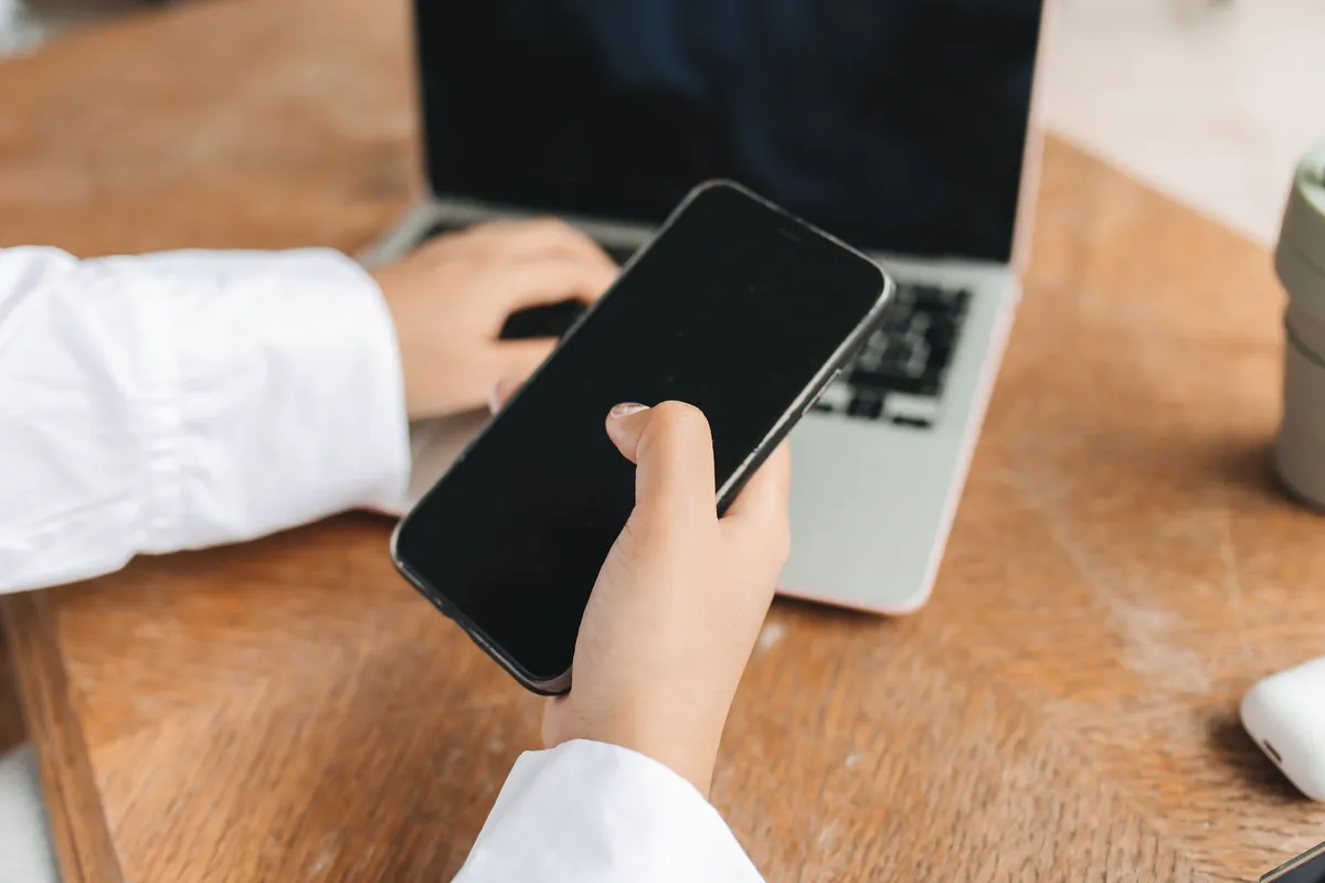 Hands holding a phone at a laptop to connect a bank account, the first step every loan app in Canada asks for