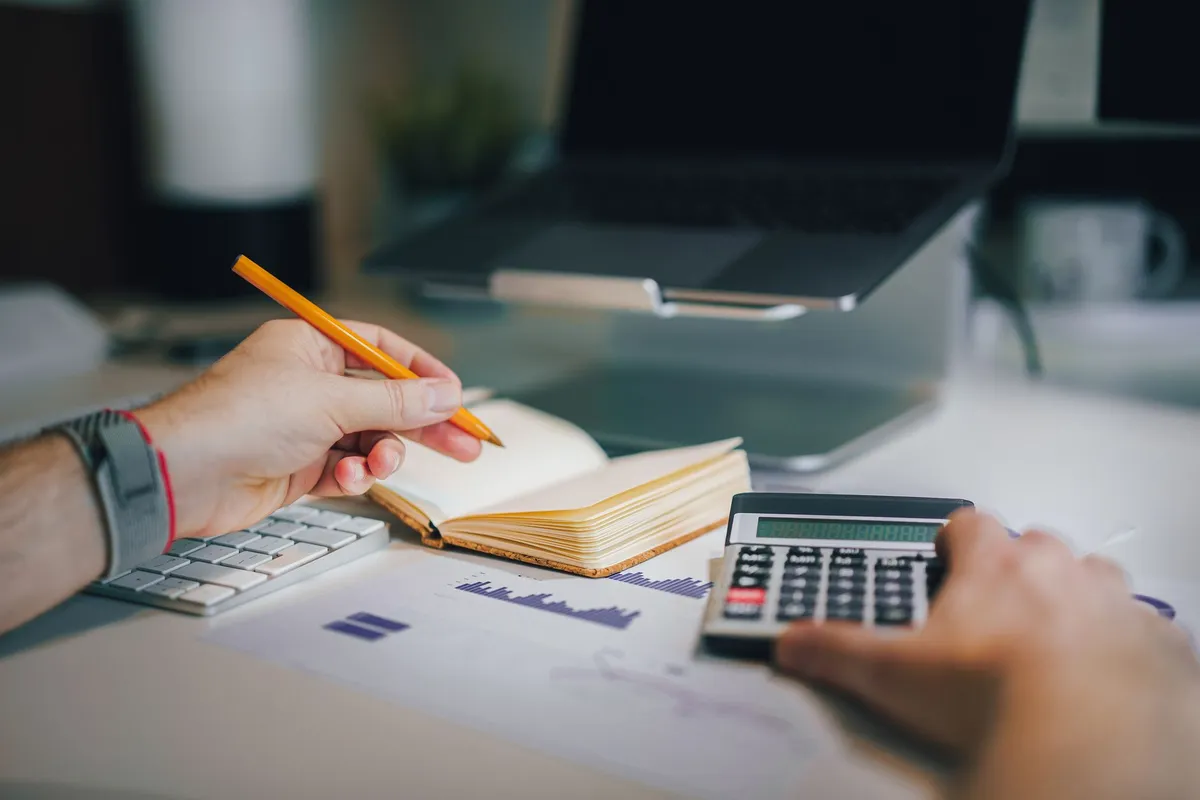 Calculator, notebook and laptop used to total three months of loan app fees in a monthly budget